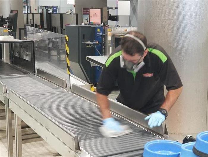 A SERVPRO employee in a warehouse cleaning on a conveyor belt. 