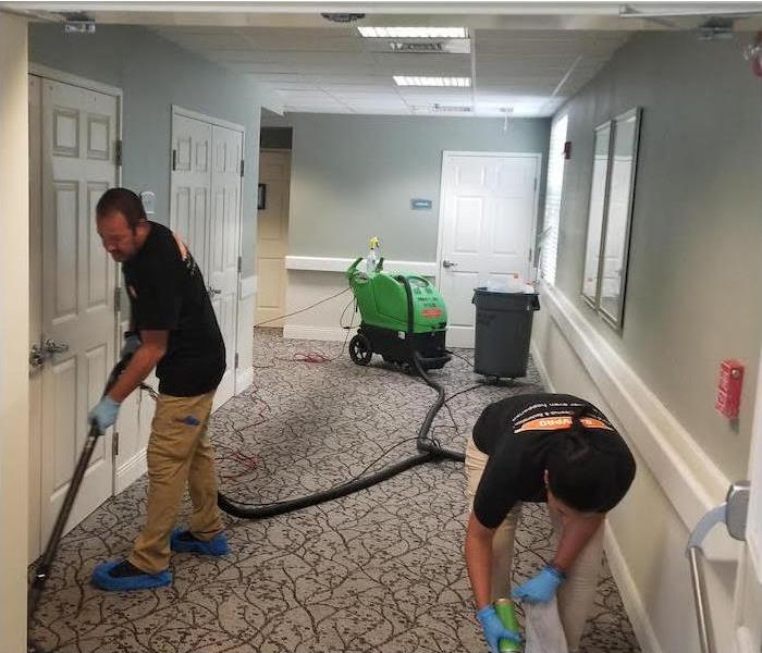 two SERVPRO employees removing water damage from a hallway