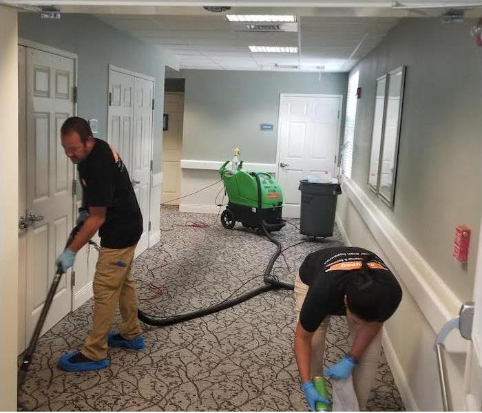 two SERVPRO employees removing water damage from a hallway